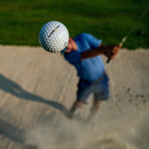 golf ball in foreground with man swinging club club in background