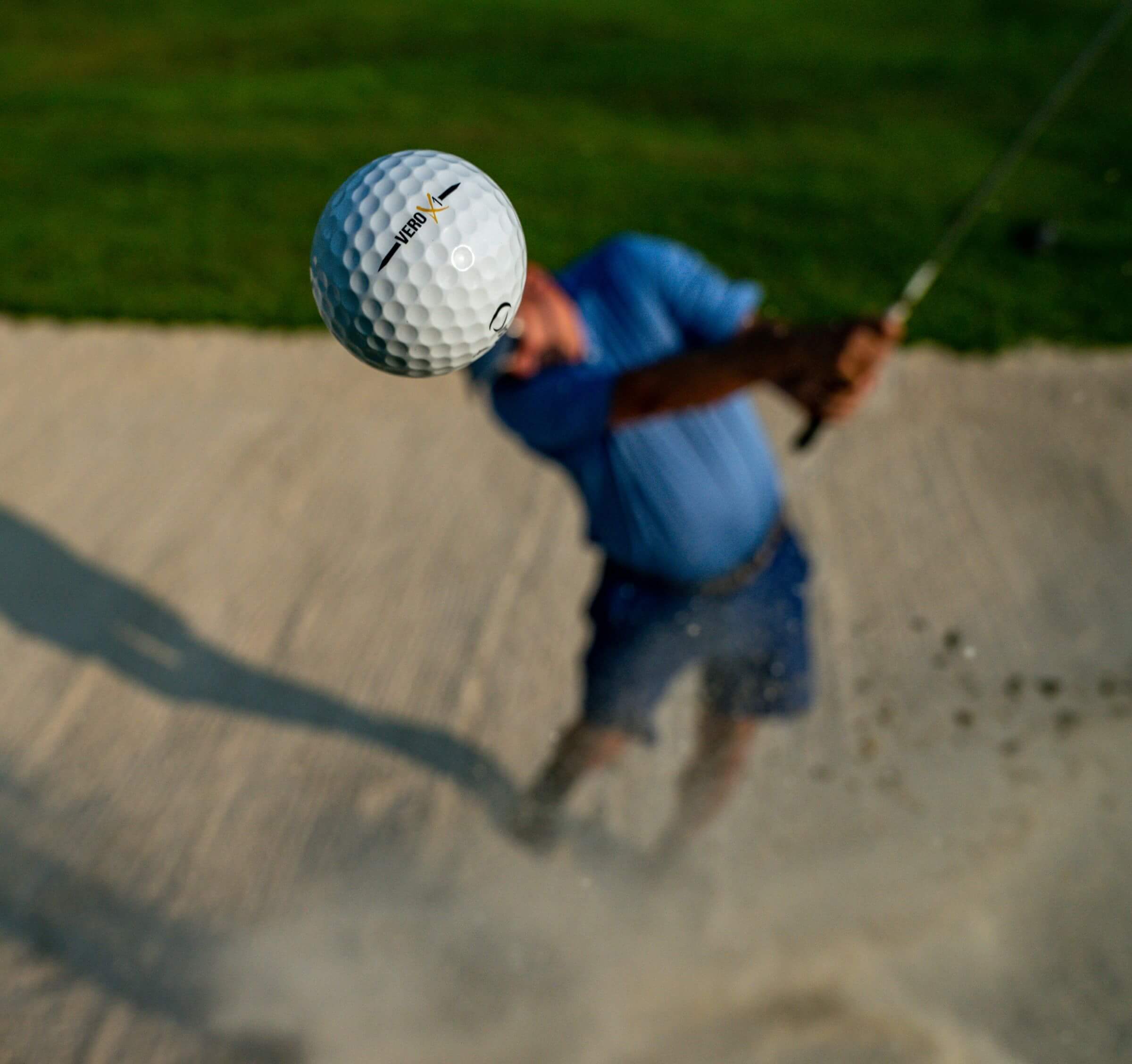 golf ball in foreground with man swinging club club in background